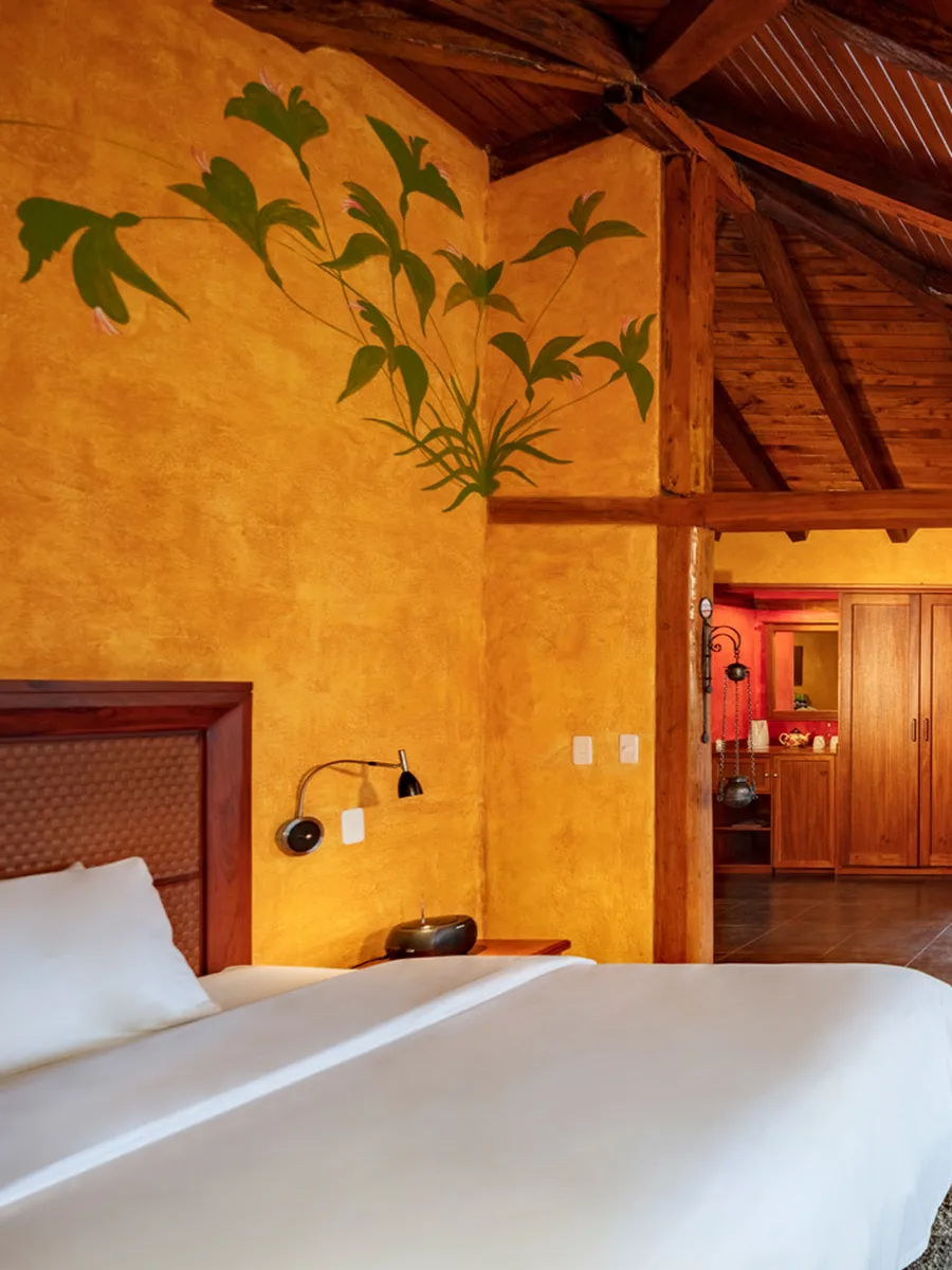 Suite con vigas de madera, sillón de cuero y ventanales al jardín en Luna Volcán